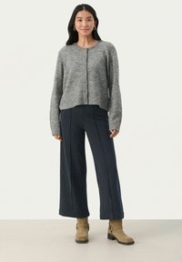Gilet en tricot gris avec un col rond et une fermeture à boutons, associé à un pantalon large à rayures navy et des bottines beige.