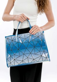 Borsa tote geometrica blu con finitura lucida, caratterizzata da motivi triangolari contornati in nero. Due manici robusti per un facile trasporto.