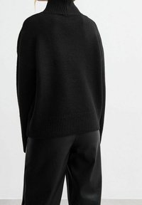 Schwarzer oversized Rollkragenpullover mit ribbelndem Kragen und Saum. Weiche Textur, lockerer Schnitt, präsentiert ein minimalistisches Design.