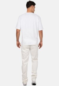 Witte t-shirt met korte mouwen en een ronde hals, gedragen met lichte broeken. De achterkant toont een gladde stof en een relaxte pasvorm.