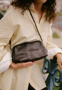 Svart läder crossbody-väska med en slät yta, rektangulär form och minimalistisk design. Har en dragkedja upptill och diskret logotyp.
