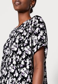 Blusa preta com padrão floral, apresentando flores brancas e roxas, mangas curtas, textura canelada e um corte solto. Destaca-se pelo design de decote em V.