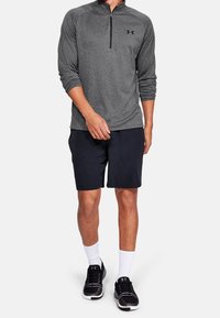 Graues langärmliges Quarter-Zip-Oberteil mit texturierter Oberfläche, kombiniert mit marineblauen Shorts und schwarzen Sportschuhen, die mit weißen Socken getragen werden.