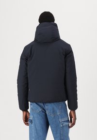 Chaqueta de plumas negra con un cuello alto y capucha, con una textura suave. Llevada con unos pantalones cargo de color azul claro.