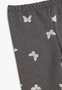 Leggings grises hechos de un tejido suave, con patrones de mariposas de purpurina plateada dispersos. Cintura elástica para un ajuste ajustable.