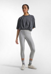 Losse grijze T-shirt met een ronde hals, gecombineerd met lichtgrijze capri leggings. Geaccentueerd met geribbelde grijze sokken en witte schoenen.
