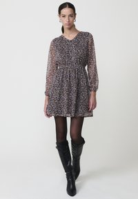 Vestido largo de manga larga y estampado floral, con un lazo en la cintura y escote en V, combinado con botas negras ajustadas hasta la rodilla.