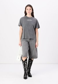 Grey oversized t-shirt with white text, grey denim shorts, and black cowboy boots featuring white embroidered accents. White handbag.