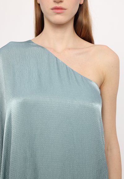 Top asimétrico de un solo hombro hecho de una tela texturizada de color azul claro con un brillo suave, que presenta un sutil patrón arrugado.