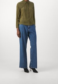Blusa a maniche lunghe con colletto in un motivo nero e giallo; pantaloni in denim blu a gamba larga; décolleté neri con punta.
