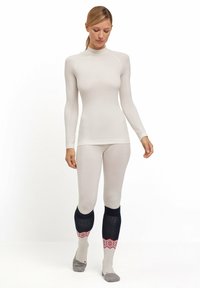 Maglietta termica a maniche lunghe e pantaloni aderenti in beige chiaro, realizzati in un morbido tessuto testurizzato; presenta dettagli a contrasto in blu navy scuro e calzini fantasia.