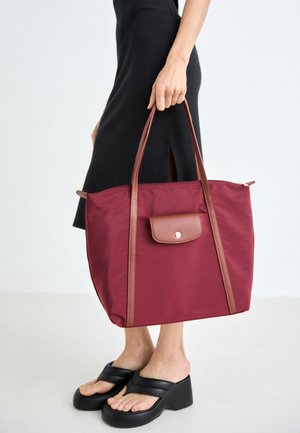 Bordeaux nylon totebag met bruin leren accenten, voorzien van twee lange handgrepen en een voorkantzak met drukknoopsluitingen. Zachte textuur.