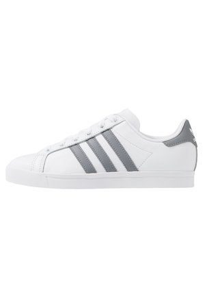 Biały niski sneaker z szarymi trzema paskami Adidas i szarą pętelką na pięcie, widziany z boku.