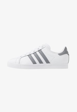 Biały niski sneaker z szarymi trzema paskami Adidas i szarą pętelką na pięcie, widziany z boku.