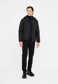 Svart vadderad jacka med huva, dragkedja och ribbade ärmslut, kombinerad med åtsittande svarta byxor och svarta sneakers.