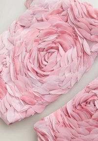 Detailný záber na ružovú tkaninu s vrstvenou textúrou pripomínajúcou lupienky, usporiadanú v kruhových kvetinových vzoroch na svetlom pozadí.