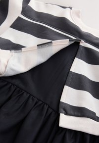 Top a righe in blu navy e bianco con colletto a coste, che si unisce a una gonna nera solida con dettagli arricciati in vita.