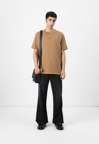 Camiseta de algodón marrón con manga corta y cuello redondo. Jeans de pierna ancha negros y zapatos negros. Lleva un bolso negro de hombro.