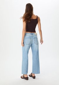 Hnědý krátký top bez rukávů a světle modré široké džíny s vybledlým povrchem, s kapsami na zadní straně a koženou nášivkou na pásku.