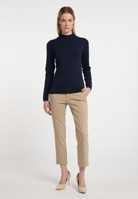 Námořnický pletený rolák spárovaný s béžovými tailored ankle kalhotami a béžovými vysokými podpatky. Oblečení má přiléhavý střih a žebrované detaily.