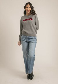 Pull gris avec l'inscription rouge "AMOUR", col rond, poignets côtelés, associé à un jean bleu clair et des bottines noires à talons. Design simple et décontracté.