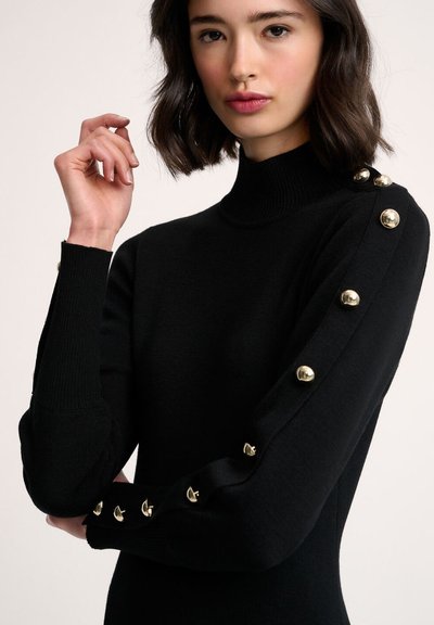 Črna turtleneck pulover s dolgimi rokavi, ki ima zlate gumbne dodatke ob rokavih. Narejen je iz gladkega, elastičnega materiala.