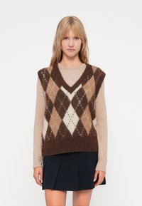 Brun og beige argyle-mønstrede strikkede vest med V-hals, båret over en lys langærmet top og parret med en mørk nederdel.