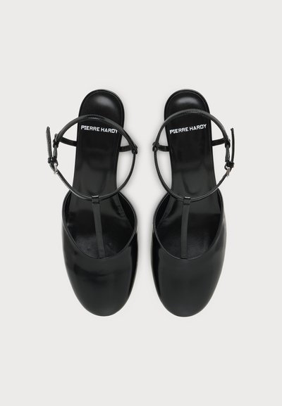 Sandales plates en cuir verni noir avec brides à la cheville et bouts carrés, estampillées Pierre Hardy sur la semelle intérieure.