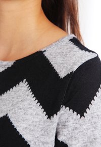 Maglione nero e grigio con un motivo a zig zag, caratterizzato da una morbida trama a maglia e un ampio scollo. Concentrati sui colori a contrasto e sui dettagli del design.