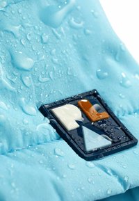 Tissu bleu clair avec des gouttes d'eau ; présente une étiquette rectangulaire en patch avec des formes bleu marine, orange, blanche et bleu clair.