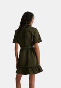 Abito verde oliva a maniche corte con vita a cintura, caratterizzato da un orlo svasato a volant e colletto strutturato. Tessuto liscio e leggero.