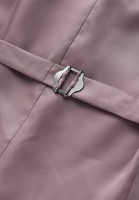 Ceinture en tissu lavande avec une boucle en métal argenté, passée dans un vêtement lavande assorti.