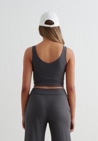 Szary sportowy biustonosz z dekoltem w kształcie litery V z tyłu i szerokimi ramiączkami, w połączeniu z szarymi, wysokim stanem spodniami. Gładka, elastyczna tkanina z minimalnym wykończeniem.