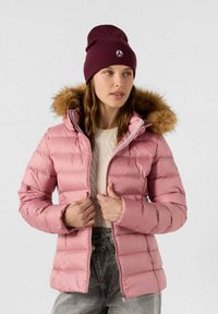 Giacca puffer rosa chiaro con cappuccio bordato di pelliccia, chiusura con zip e polsini a coste, abbinata a un berretto bordeaux e a un maglione strutturato.