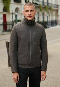 Braune Lederjacke mit hohem Kragen, Reißverschluss vorne und seitlichen Taschen. Verfügt über eine glatte Textur und ein minimalistisches Design.