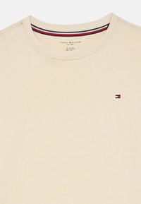 Beige crew neck t-shirt with small Tommy Hilfiger flag logo on the chest and striped collar detail inside the neckline.
