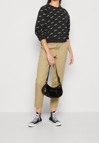Felpa nera con stampa del logo bianca, chinos beige, borsa a tracolla nera in vernice e sneakers alte nere con lacci bianchi.