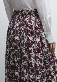 Bloemmotiefrok met plooien; heeft een donkerbordeaux en paarse print op een crèmekleurige achtergrond. Gerimpelde tailleband en textiel met structuur.