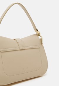 Beige leather handbag with flap closure, short handle, gold hardware, and subtle embossed brand name "FURLA" on front pocket.