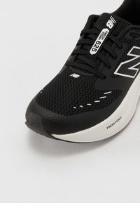 Musta urheilujalkine verkkomateriaalista, pyöreä kärki, valkoisia yksityiskohtia ja "FRESH FOAM" -logoa pohjassa vaimennusta ja tukea varten.