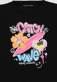 T-shirt nera con un vivace design grafico caratterizzato da testo e motivi in rosa, blu, arancione e bianco. Elementi notevoli includono un fiore e una tavola da surf.