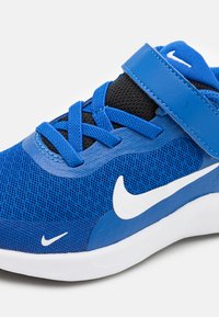 Las zapatillas Nike azules cuentan con una parte superior de malla, acentos negros en contraste, cordones y una correa de Velcro. Un logotipo de swoosh blanco se exhibe de manera prominente.