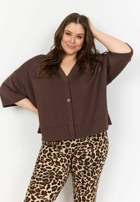 Brun knapptopp med v-ringning och breda ärmar, kombinerad med leopardmönstrade byxor i en beige och svart design. Mjukt material.