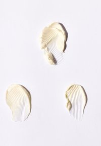Trois traces distinctes de lotion blanche crémeuse avec des crêtes texturées sur une surface blanche lisse.