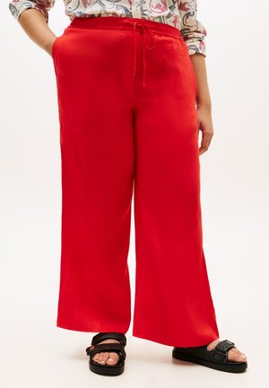 Person wearing bright red wide-leg pants with drawstring waist, patterned shirt, and black open-toe sandals on a plain light background.