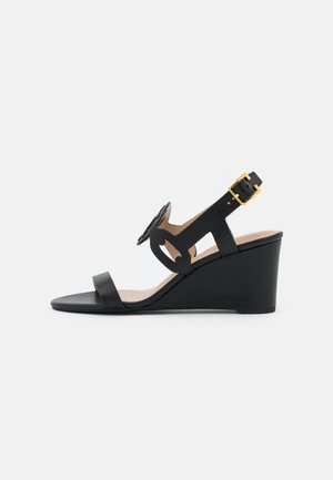 Zwarte sleehak sandaal met een open teen, voorzien van een gestructureerd riemontwerp, verstelbare enkelgesp en een glad voetbed. Gouden metalen accenten.