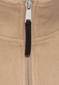 Giacca in pile beige con zip frontale dotata di cursore argentato, nastro zip nero a contrasto e tessuto strutturato.