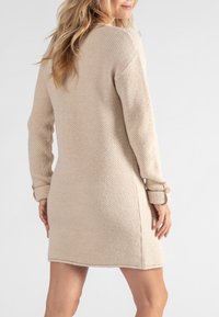 Beige Strickkleid mit entspanntem Schnitt, langen Ärmeln mit umgeschlagenen Manschetten und Knopfakzenten. Durchgehend strukturierter Stoff, bis zur Mitte des Oberschenkels.