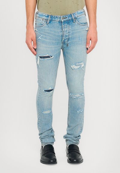 Lichtblauwe denim jeans met gescheurde details, slim fit, vijf zakken, vervaagde afwerking en een middellange taille. Draagt met zwarte schoenen.