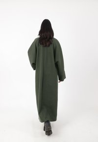 Lange, oversized, donkergroene jas van zachte stof met brede mouwen en een losse silhouet, voorzien van een rechte zoom en zonder zichtbare sluitingen.